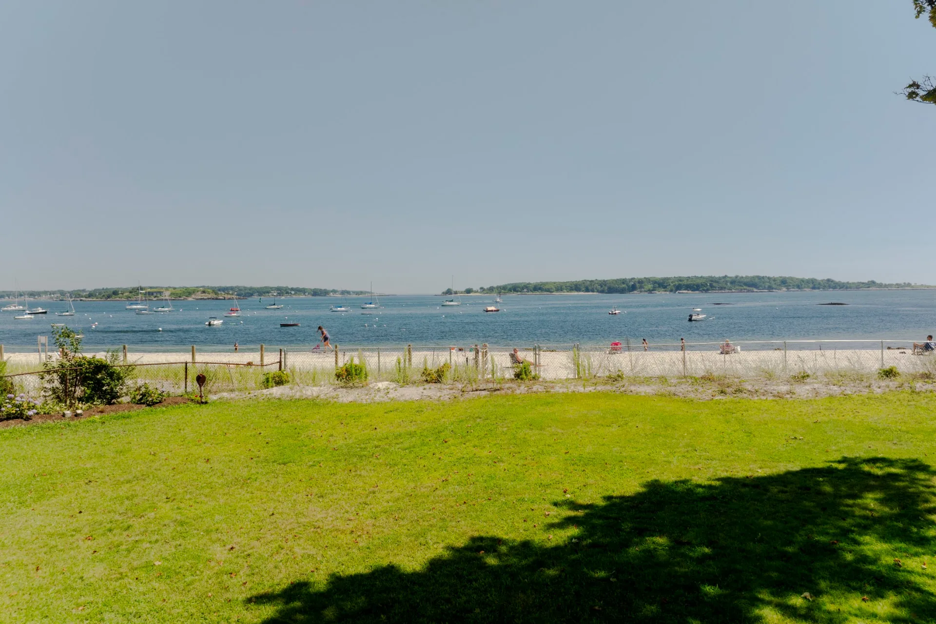 The fenced lawn and private beach frontage of the Oceanfront Retreat, with sailboats on Casco Bay